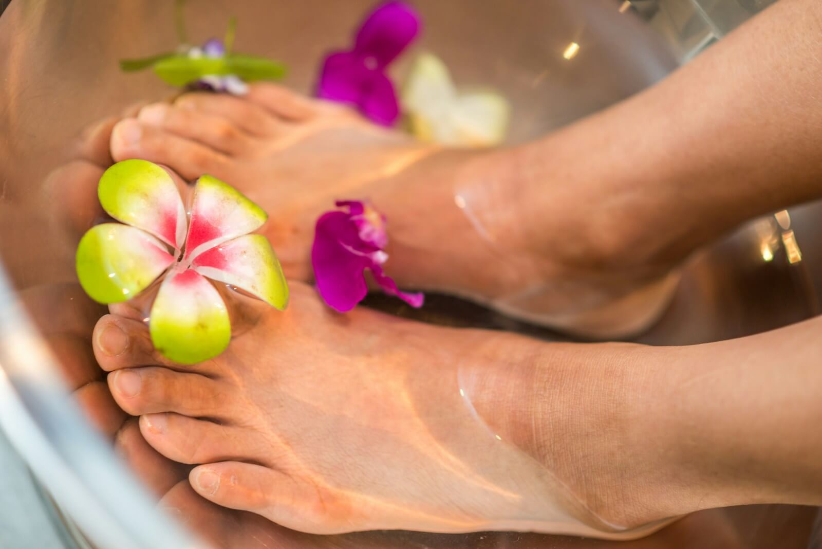 Relaxing feet soaking in a bucket of water with floating flowers